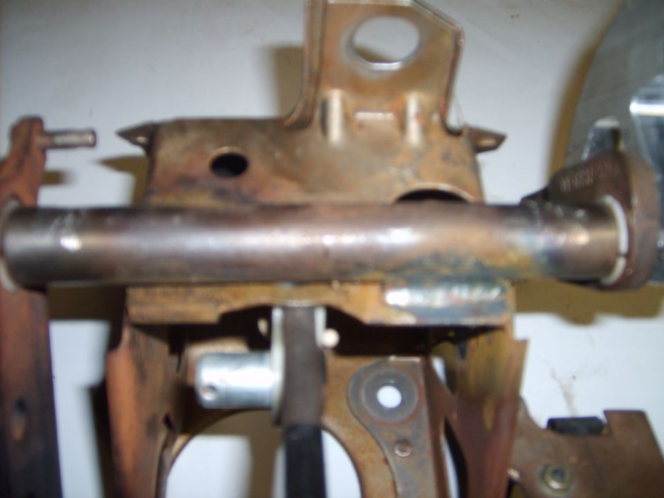 Rusty steel pedal bracket assembly with cross shaft and zinc pivot pin on white background