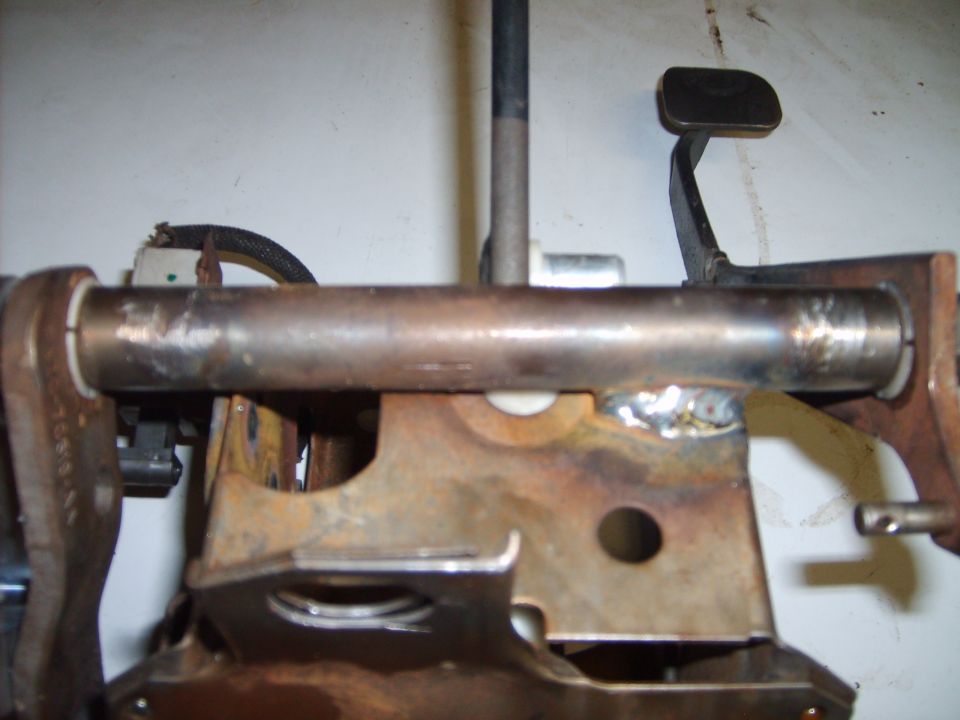 Welded steel cross tube on rusty pedal support bracket with small black pedal arm