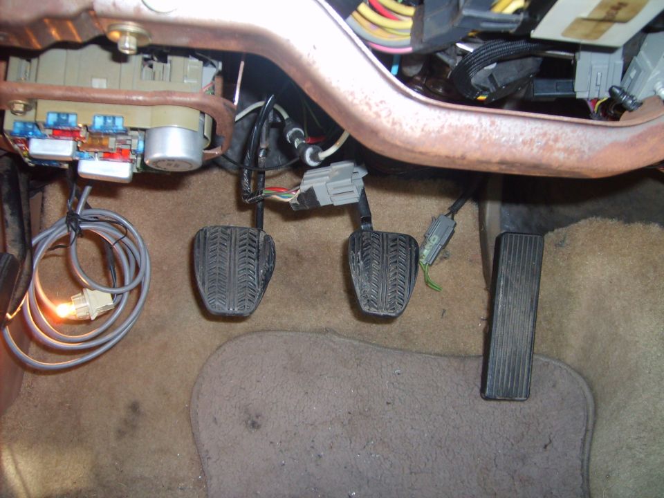 Footwell with clutch and brake pedals installed, dash open showing fuse panel and wiring