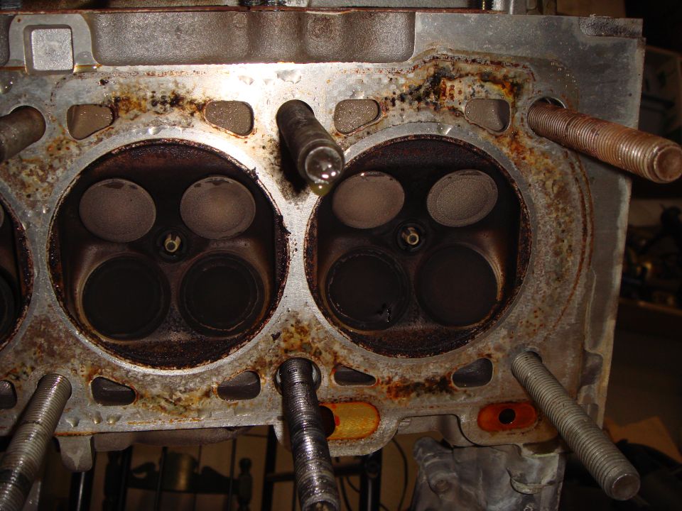 Cylinder head deck showing two four-valve combustion chambers with carbon buildup and rust.