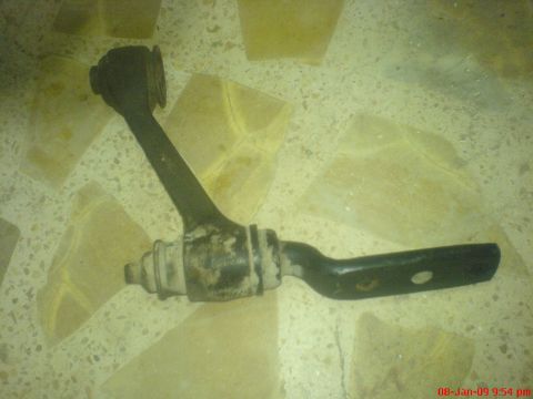 1992 Ford Crown Victoria - A black suspension control arm with rubber bushings is shown lying on a speckled floor.