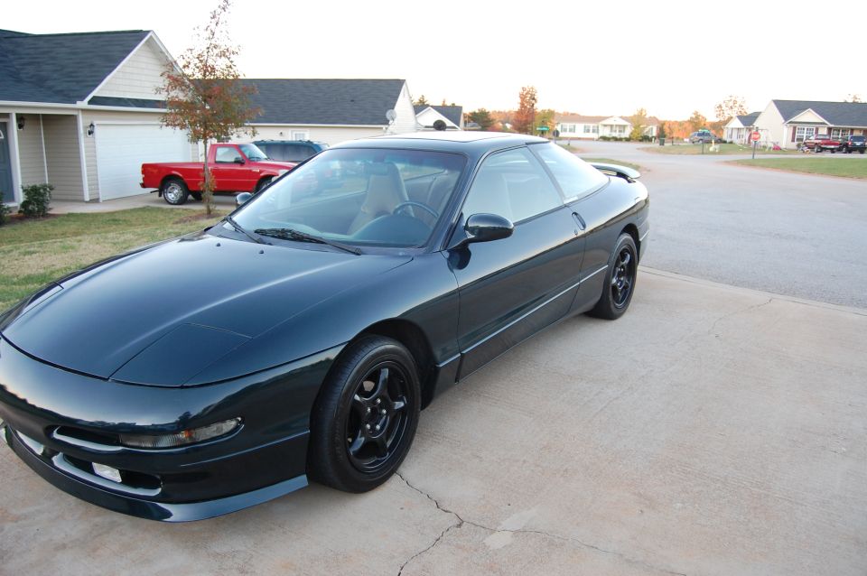 1996 Ford Probe coupe, dark green, parked on concrete driveway, suburban setting.