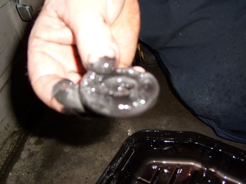 1972 Ford Ranchero - A hand holds a dark, metallic object covered in a thick, greasy substance, with a black pan filled with dark liquid in the background.