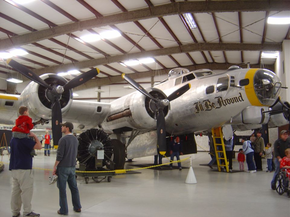Silver B-17 Flying Fortress airplane in a hangar with people viewing it.
