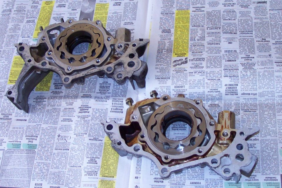 Two aluminum oil pump housings with covers off showing gerotor rotors, on newspaper