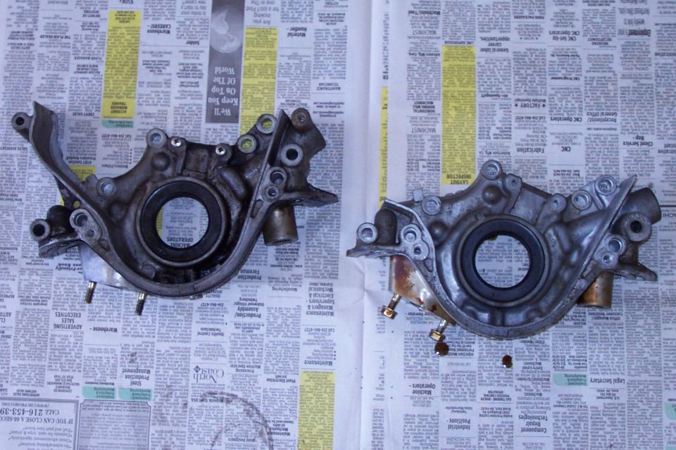 Two aluminum oil pump front cover housings with crank seals, side by side on newspaper
