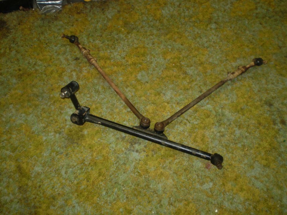 Two steering linkage assemblies on a green carpeted surface.