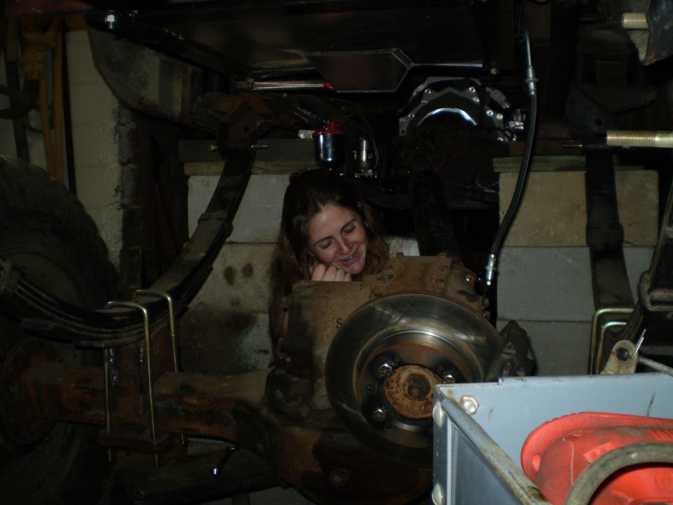 Woman with braces smiles while leaning on vehicle suspension and brake assembly.