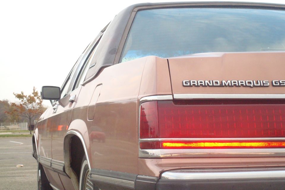 Rear quarter of a rose-colored Mercury Grand Marquis GS with full-width taillight