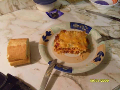 1989 Ford Bronco - A slice of lasagna sits on a plate next to a piece of bread. A fork and knife are also visible on the table.