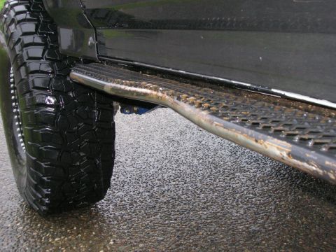 1996 Ford Bronco - A close-up, low-angle view of the driver's side of a black SUV, focusing on the large, aggressive tire and the diamond-plate running board.…