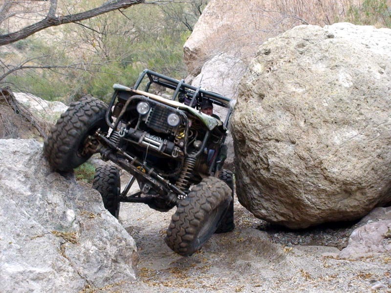 Caged camo Bronco with winch flexing between boulders on a desert crawling trail