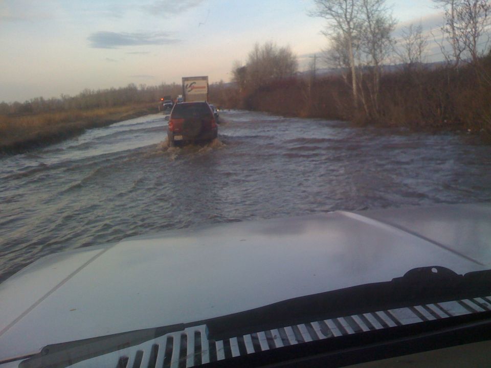 Red SUV driving through a flooded road, seen from the perspective of another vehicle.