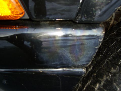 1972 Ford Ranchero - A close-up, low-angle shot of the rear corner of a black vehicle, showing damage and reflection on the bumper. A portion of a tire tread is…