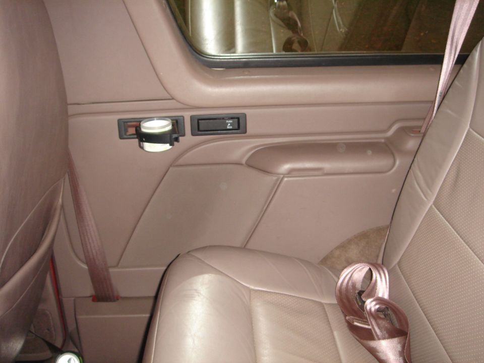 Interior of a vehicle showing tan leather seat and door panel with cup holder and seatbelt.