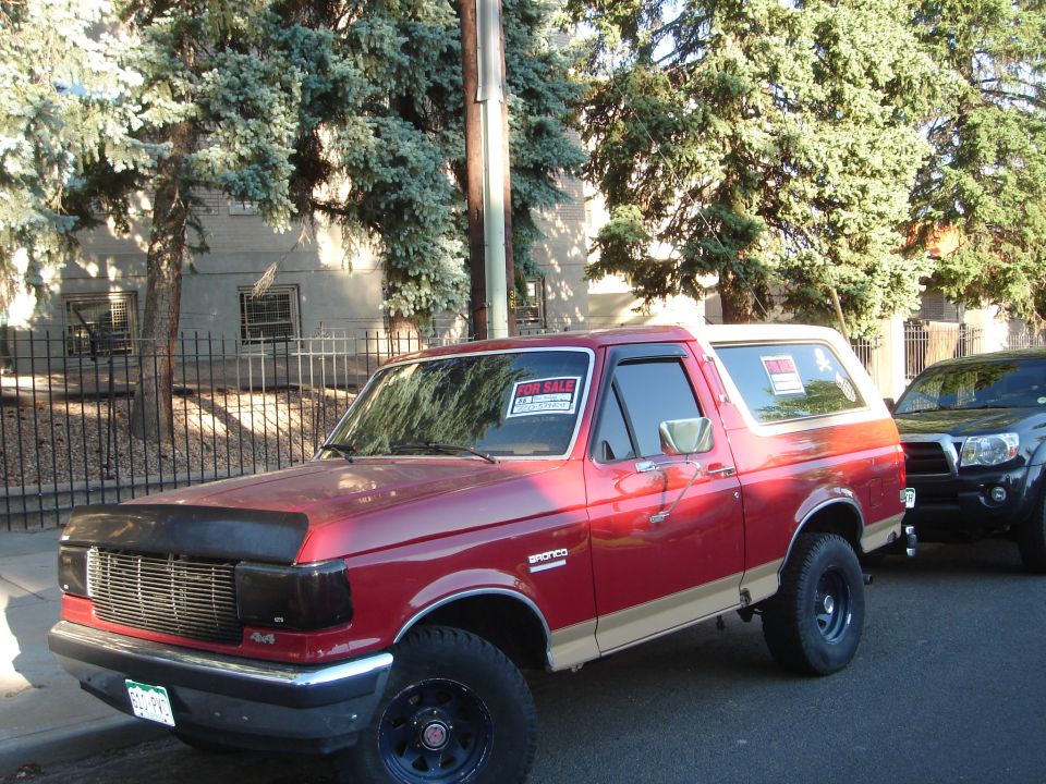 Red 1994 Ford Bronco parked on street with a "For Sale" sign.