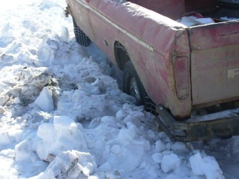 1978 Ford F-150 - A red pickup truck is stuck in a snowdrift, showing its rear side and tire.