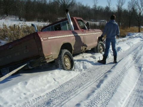 1978 Ford F-150 - A maroon 1978 Ford F-150 is stuck in a snowy ditch, its dual exhaust pipes visible above the snow line.