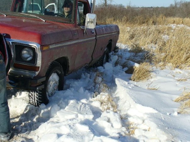 Red 1978 Ford F-150 stuck in deep snow, front 3/4 view, driver visible
