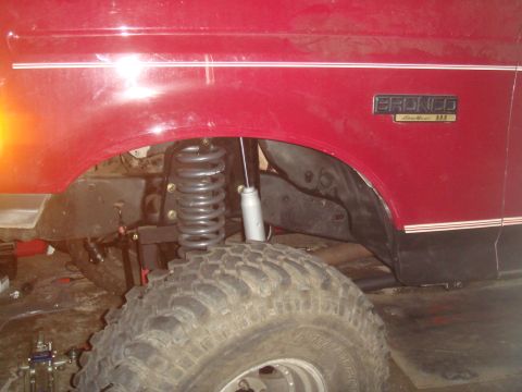 1992 Ford Bronco - Close-up of the fender and suspension of a red 1992 Ford Bronco, showing the "Bronco" badging and lifted components.