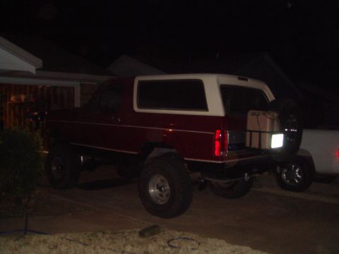 1992 Ford Bronco - A red and white SUV is parked outside at night, with a spare tire and a gas can mounted on the rear.