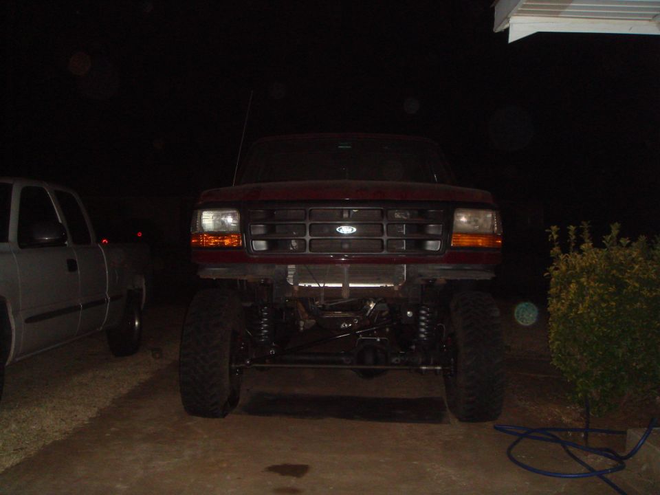 Red 1992 Ford Bronco, front view, lifted suspension, aftermarket grille, parked next to a silver pickup truck