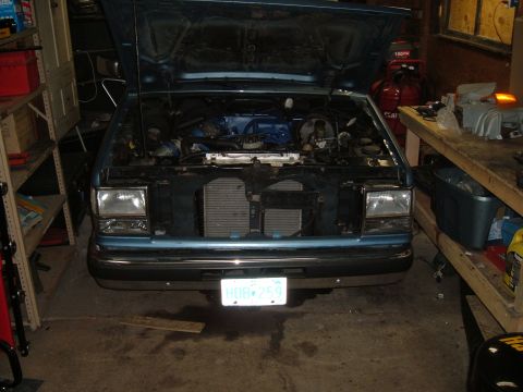 1990 Ford Ranger - The front of a light blue Ford Ranger is shown with its hood up, revealing the engine compartment and radiator.