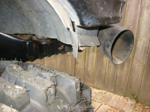 1995 Ford Bronco - A close-up view of a vehicle's large tire and exhaust pipe against a wooden fence.