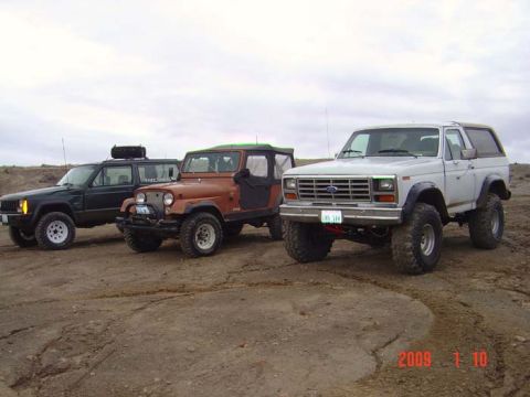 1983 Ford Bronco - A white 1983 Ford Bronco is parked in a dusty, outdoor lot alongside two Jeeps.