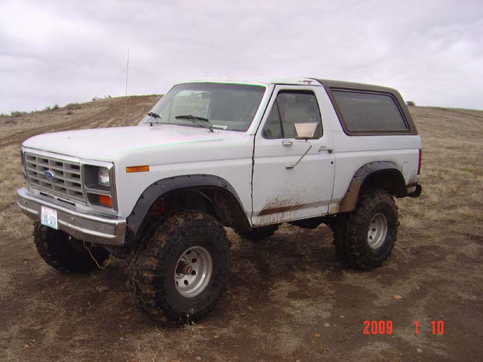White Ford Bronco with aftermarket wheels and tires parked on a dirt hill