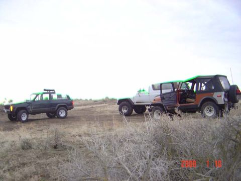 1983 Ford Bronco - Multiple off-road vehicles are parked on a dirt track under a bright sky.