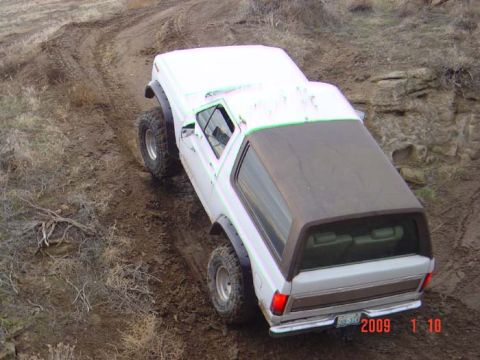 1983 Ford Bronco - A white SUV navigates a challenging off-road trail with steep inclines and loose dirt.