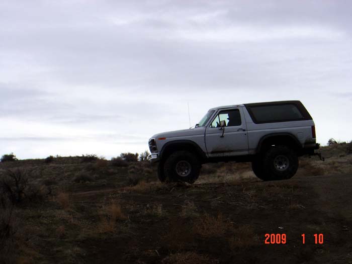 Silver Ford Bronco on a dirt hill under a cloudy sky
