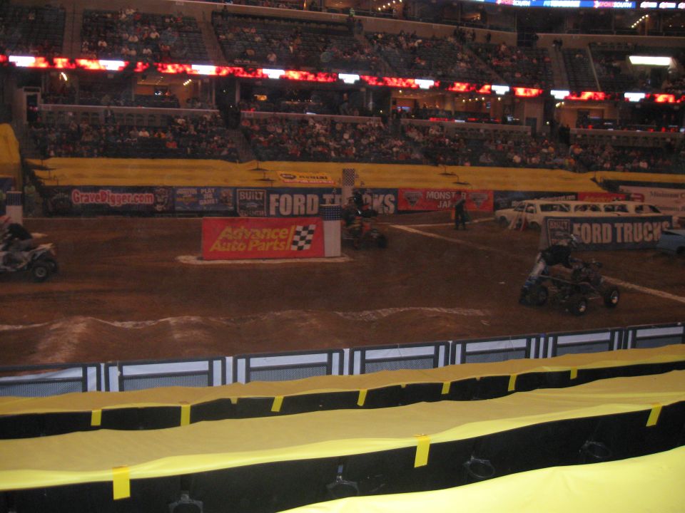 Monster Jam event in an arena with Ford Trucks signage and some ATVs on the dirt track