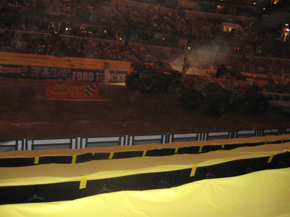 Monster trucks on dirt track in stadium with Ford Trucks banner