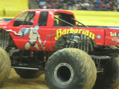 1994 Ford Bronco - A red monster truck with the name 'Barbarian' emblazoned on its side is captured in motion.