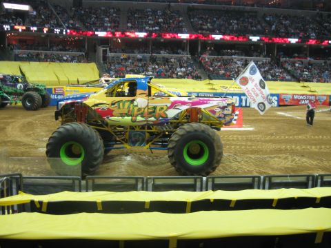1994 Ford Bronco - A colorful Monster Jam truck is on display in an arena, with a crowd in the background and another monster truck nearby.