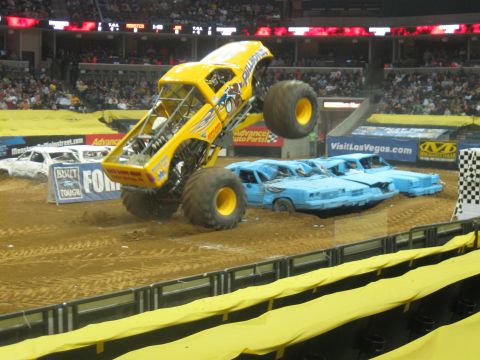 1994 Ford Bronco - A monster truck soars through the air during a competition, crushing a line of blue cars below.