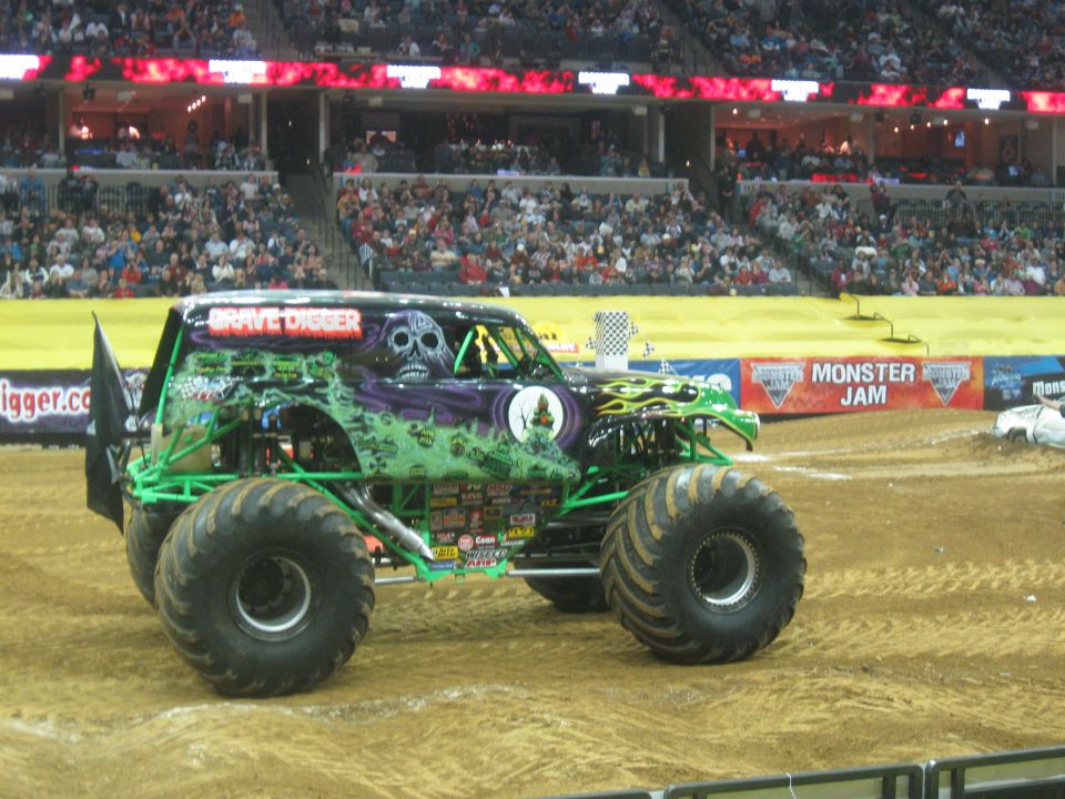 Monster truck with Grave Digger graphics and large tires sits on dirt track in arena