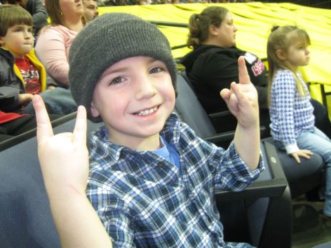 1994 Ford Bronco - A young boy wearing a beanie and plaid shirt smiles while making hand gestures at an event.