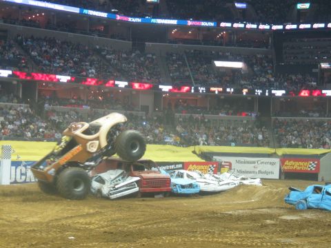 1994 Ford Bronco - A monster truck event with a truck crushing several cars in an arena filled with spectators.