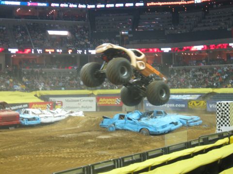 1994 Ford Bronco - A monster truck soars through the air above a pile of crushed cars during a Monster Jam event.