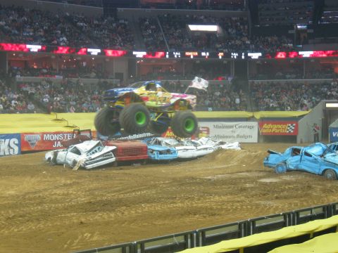 1994 Ford Bronco - A monster truck performs a jump over a collection of crushed cars during an event.