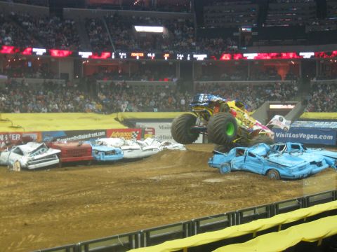 1994 Ford Bronco - Monster truck performs a jump over a pile of destroyed cars during an event in a stadium.
