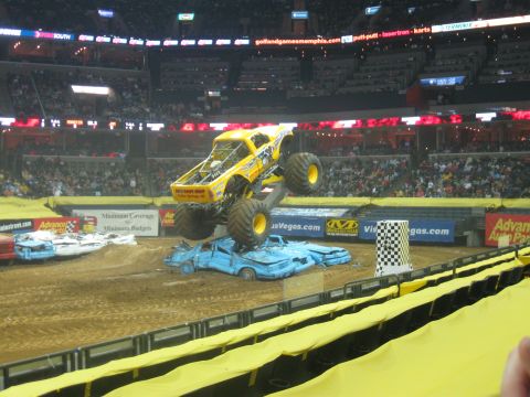 1994 Ford Bronco - Monster truck event with a yellow truck jumping over several crushed cars in an arena.