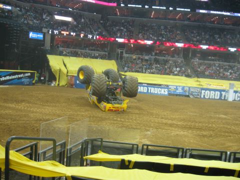 1994 Ford Bronco - A monster truck is shown upside down on a dirt track during an event, with a large crowd watching.