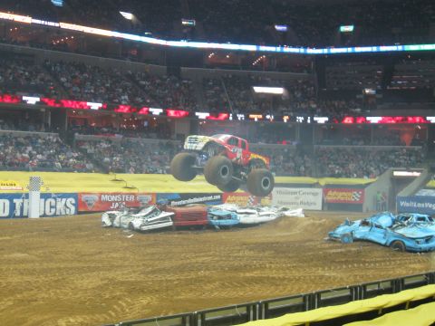 1994 Ford Bronco - A monster truck soars through the air above a pile of mangled cars during a competition.