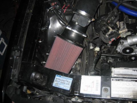 1996 Ford Thunderbird - Close-up view of a vehicle's engine bay, an aftermarket air intake system and a Ford emissions label.