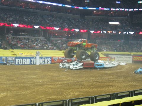 1994 Ford Bronco - Monster truck performs a jump over a pile of crushed cars during an event. "Built Ford Trucks" is displayed on a banner.