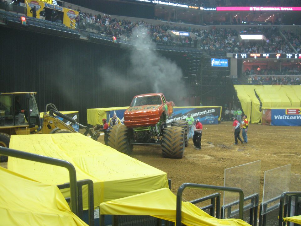 Red monster truck with large tires emitting smoke, viewed from the front